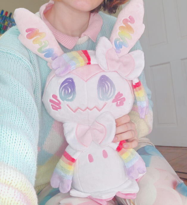 image of a person holding a pastel rainbow colored handmade sylveon-mimikyu plush